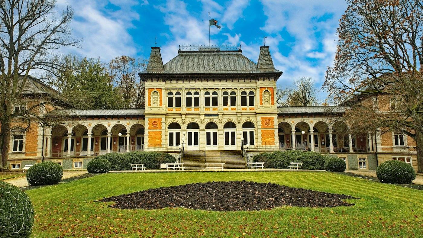 Yellow historic bathhouse with arcades behind a lawn