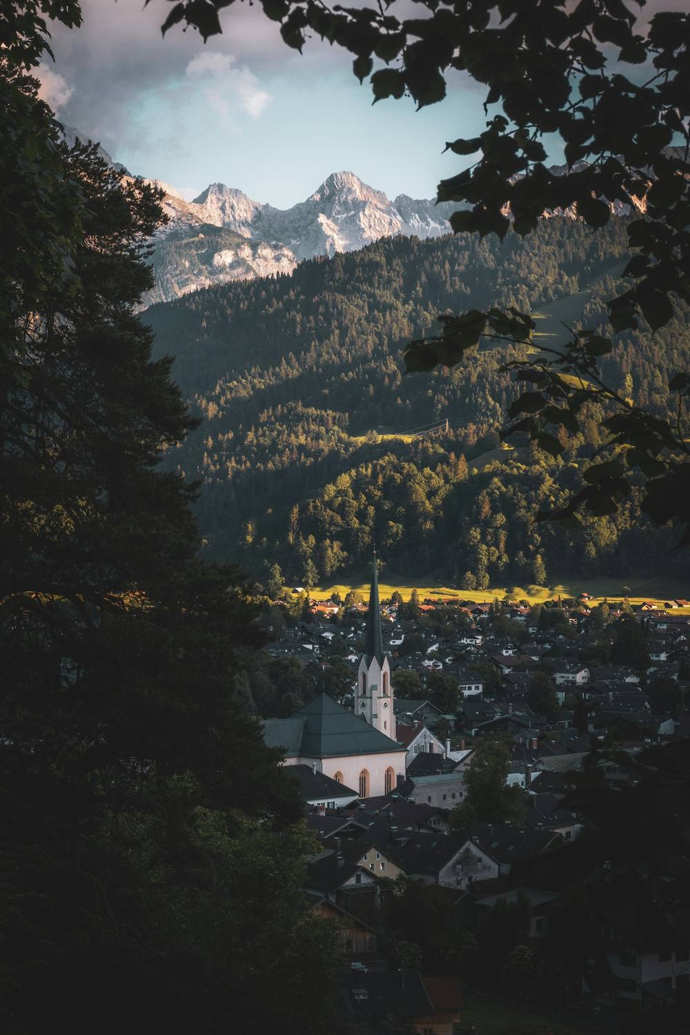 View through trees to a town with a church and peaks