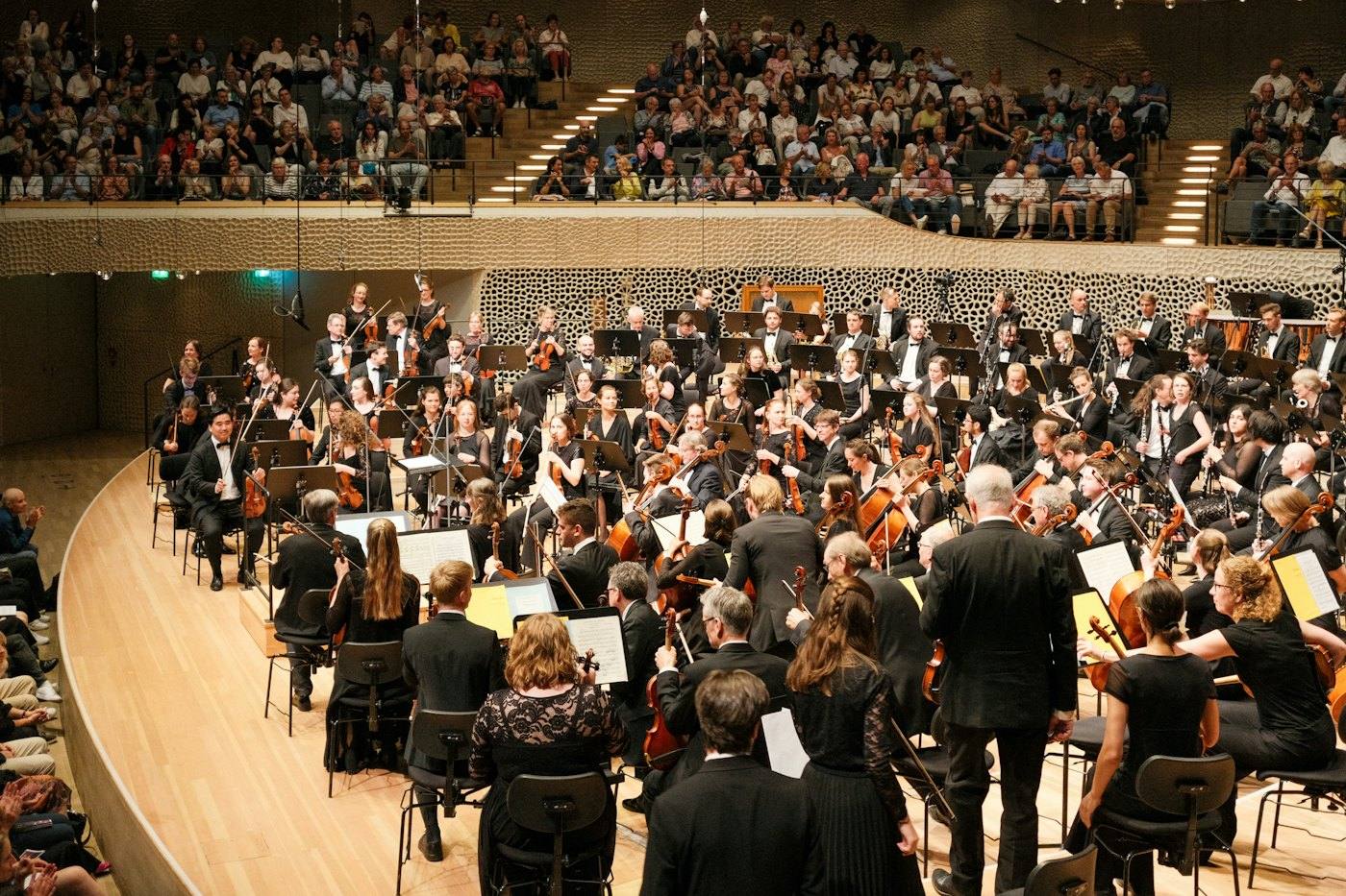 Large orchestra and conductor on stage, audience all around